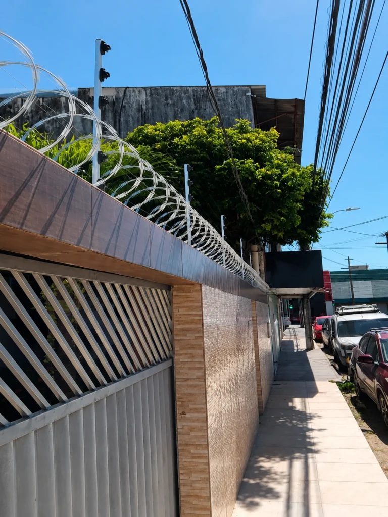Instalação de cerca elétrica industrial com concertina galvanizada realizada pela Força e Luz em residência no bairro Alecrim, Natal RN, proporcionando proteção perimetral reforçada.