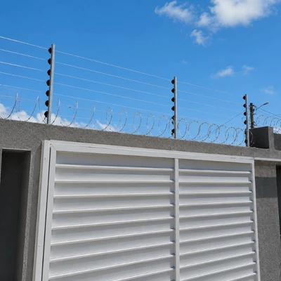 Instalação de cerca elétrica com concertina realizada pela Força e Luz no bairro Barro Vermelho, em Natal/RN, utilizando arame de aço inox, concertina galvanizada, hastes de alumínio com 6 isoladores, central de choque de 18 mil volts, bateria, sirene e aterramento.