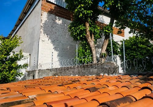 Instalação de cerca elétrica com concertina realizada pela Força e Luz no bairro Capim Macio, em Natal/RN, utilizando arame de aço inox 0,90 mm, concertina galvanizada de 30 cm, hastes de alumínio com 6 isoladores, central de choque de 18 mil volts, bateria, sirene, aterramento e placas de advertência.